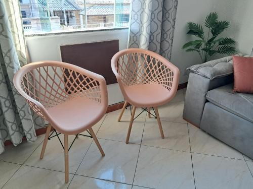 two pink chairs in a living room with a couch at Refúgio do Abricó - apto com ar e garagem in Rio das Ostras