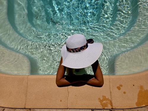 une femme dans un chapeau assise devant une piscine dans l'établissement Casa Agave-Charmante maison avec étage offrant des prestations de qualité., à Sillans-la-Cascade