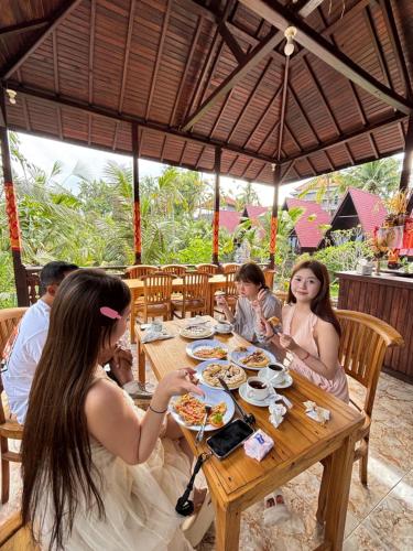 a group of people sitting at a table eating food at Kelingking Terrace Cottage in batumadeg
