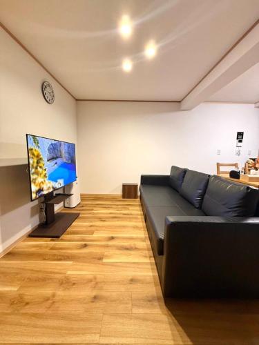Una sala de estar con un sofá negro y un televisor de pantalla plana. en 熱海網代くす亭, en Atami