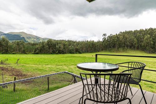 a table and chairs on a deck with a view of a field at Las Cabañas by PMJ in Cayambe