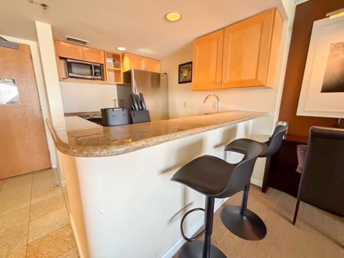 a kitchen with a counter and a bar with two stools at Ilikai Apt 2127 - Spacious Studio with Spectacular Ocean & Harbor Views in Honolulu