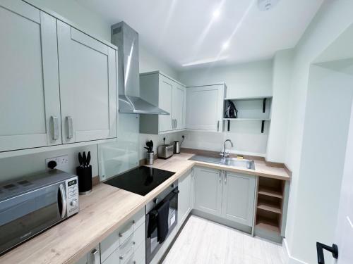 a kitchen with white cabinets and a sink and a microwave at The Octavius Apartment - Huntingdon Town Centre - Designed for Contractors & Professionals - Free WiFi - Smart TV - Fully Equipped Kitchen - Ideal for Long Work Stays in Huntingdon