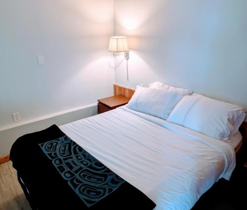 a bedroom with a bed with white sheets and a lamp at Gordie's Inn & Suites in Alert Bay