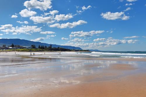 a beach with people walking on the sand and the ocean at Woonona Stays in Woonona