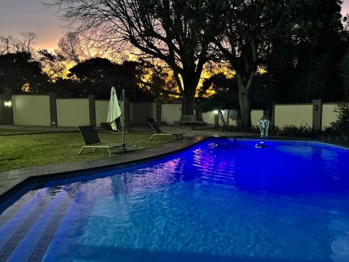 a blue swimming pool with two chairs and an umbrella at Adinkra Boutique Hotel in Johannesburg