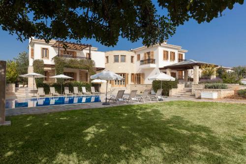 a large house with a yard with chairs and umbrellas at Aphrodite Hills Rentals - Elite Villas in Kouklia