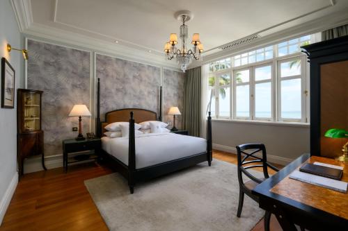 a bedroom with a bed and a table and a chandelier at Eastern & Oriental Hotel in George Town