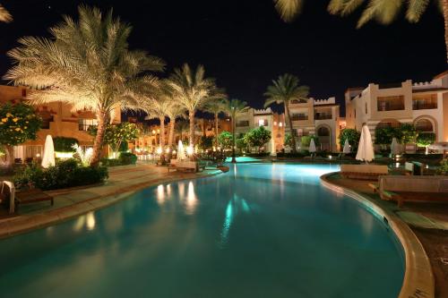 una piscina por la noche con palmeras y edificios en Rehana Royal Beach Resort - Aquapark & Spa - Family & Couples Only, en Sharm El Sheikh