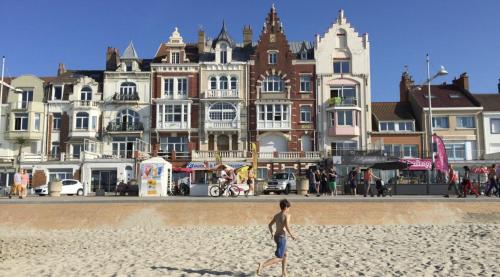 Ein Junge, der am Strand vor Gebäuden läuft in der Unterkunft La Plénitude face à la mer in Dunkerque
