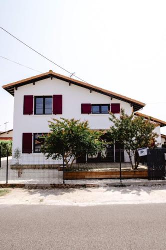 a white house with red windows and a fence at Maison Castor, balnéo et billard chez Ivona Vacances in Mimizan