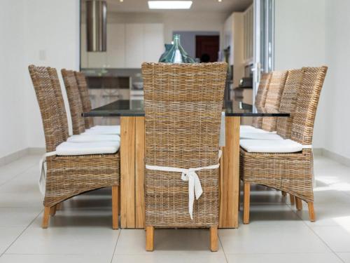 a dining room table with wicker chairs and a kitchen at Naledi@53 Private Game Farm in Brits