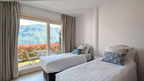 two beds in a room with a large window at Villa Selva in Bellagio