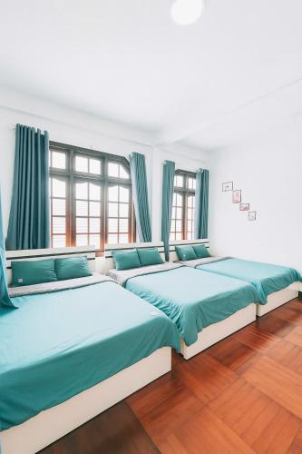 three beds in a room with blue curtains at Dona Hotel in Da Lat
