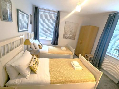 a bedroom with two beds and two windows at Chichester City Centre 2 Bedroom Flat I Ground Floor with Underground Parking I Chichester Holiday Properties in Chichester