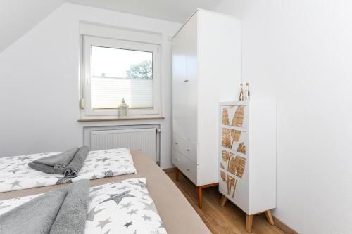 a white bedroom with a bed and a window at Ferienwohnungen Haus Boje in Neuharlingersiel
