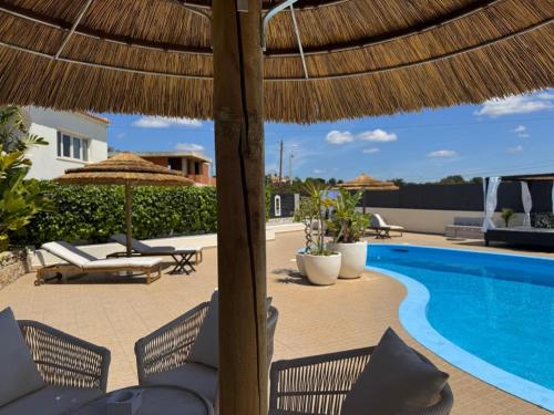 a patio with chairs and a swimming pool with a straw umbrella at Cegonha Villa powered by Cegonha Resort- Private swimming pool & air con in Albufeira