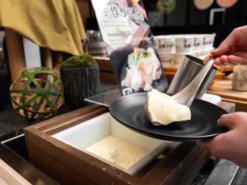 a person holding a plate with a piece of cheese at Super Hotel Kyoto Shijokawaramachi in Kyoto