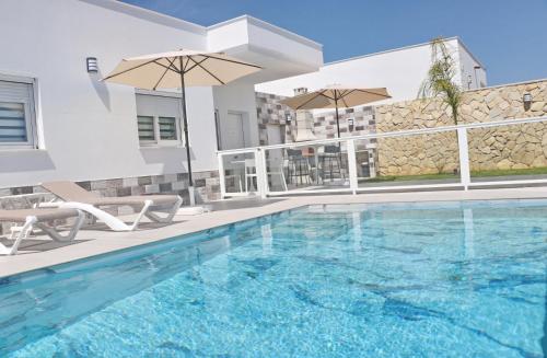 a pool with chairs and umbrellas next to a building at El Rincon de Samuel in Conil de la Frontera