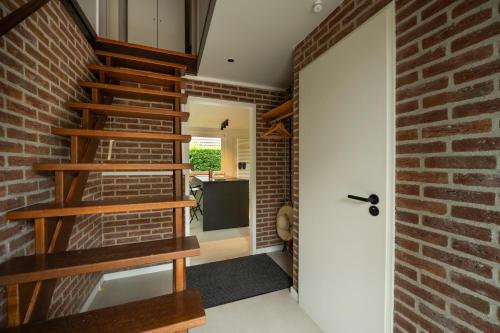a brick walled hallway with wooden stairs and a door at De Duiker in Wolphaartsdijk