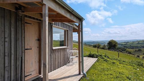 a wooden cabin with a porch and a chair on a hill at The Fold - Unique Cabin Nestled in Nature in Llangernyw