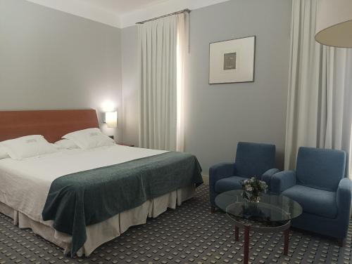 a hotel room with a bed and two blue chairs at Gran Hotel Albacete in Albacete