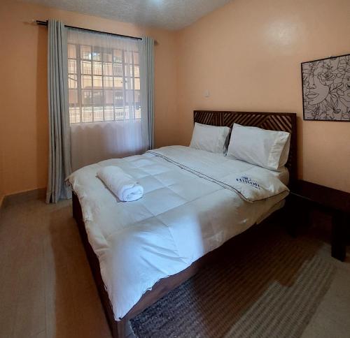 a bedroom with a bed with white sheets and a window at Staycation with Karimi in Embu