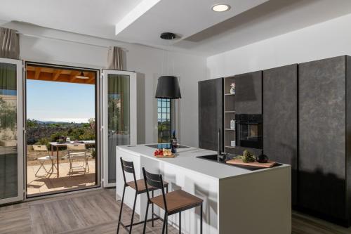 a kitchen with a white counter and chairs and a large window at Dimora degli Ulivi 10 Emma Villas in Noto