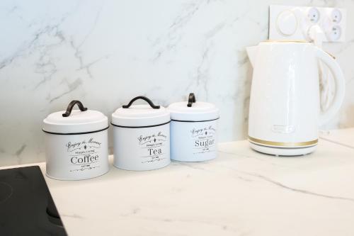 four white coffee cans sitting on a counter with a coffee pot at Apartament Valentino Bussines Haven & Family in Kielce