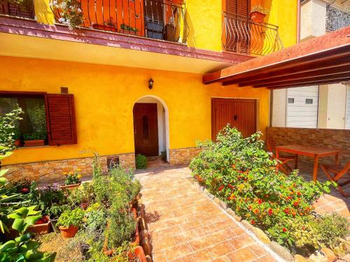 a yellow house with a patio with flowers and plants at Open Space s'Ollastu con WiFi, Patio e Aria Condizionata in Cardedu