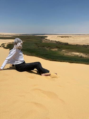 a woman sitting on the sand in the desert at Eyad Pyramids view in Cairo