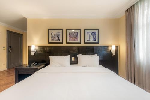 a bedroom with a large white bed with three pictures on the wall at Rockefeller by Slaviero Hotéis in Curitiba