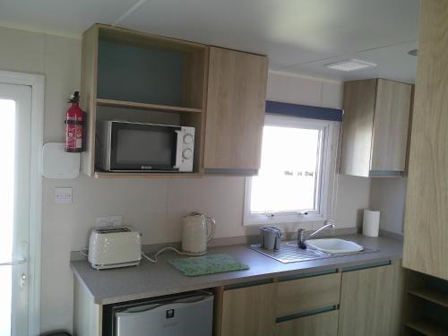 a small kitchen with a sink and a microwave at Kingfisher New Horizon Firs 8 Berth Blow Heated in Ingoldmells