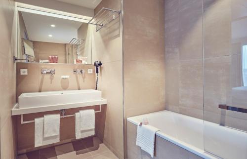 a bathroom with a sink and a tub and a shower at Mondorf Parc Hotel & Spa in Mondorf-les-Bains