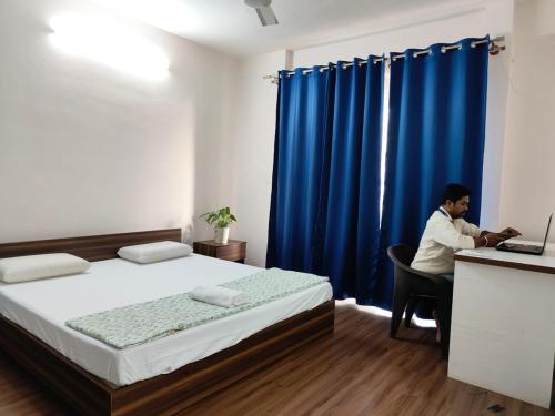 a man sitting in a chair in a room with a bed at Spacious 3 BHK inHigher flr with Sunset, Lake View in Bengaluru