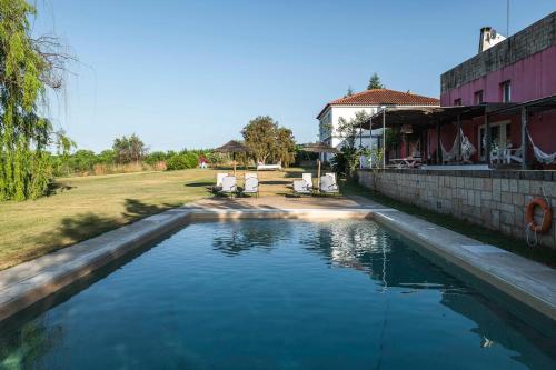 a swimming pool with two chairs and a house at Casa das Jardas in Idanha-a-Nova