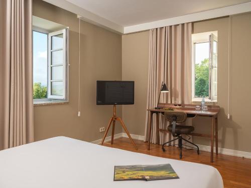 a bedroom with a bed and a desk and a television at Forrester Essence Douro Hotel - by Unlock Hotels in Alijó