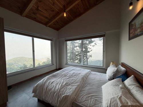 a bedroom with two large windows and a bed at Haven Lodge KhairaGali - Pine Ridge Residences #3 in Khaira Gali