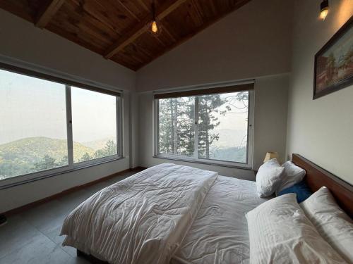 a bedroom with two large windows and a bed at Haven Lodge KhairaGali - Pine Ridge Residences #3 in Khaira Gali