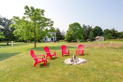 four red chairs sitting around a fire pit in a field at Walk to Lake Kelleys Island Gem with Deck! in Kelleys Island