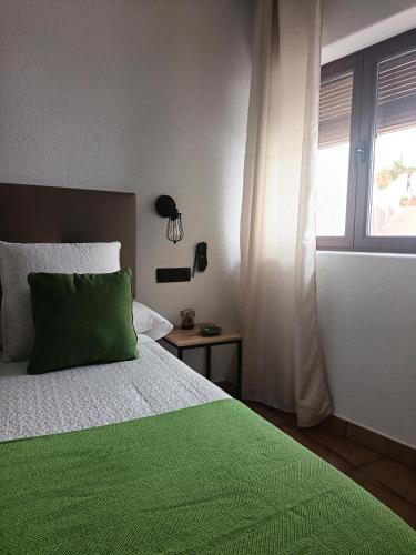 a bedroom with a bed with a green pillow and a window at La Troje Pensión in Lucainena de las Torres