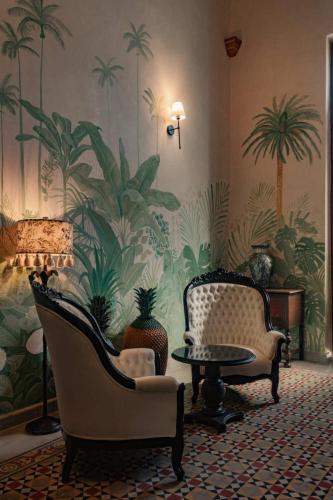 a living room with two chairs and a table and palm wallpaper at Casa Esther - Parque Santiago in Mérida