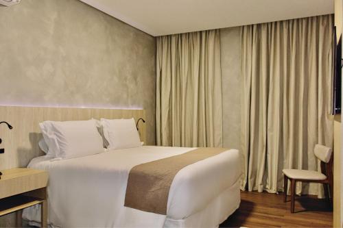 a hotel room with a white bed and a chair at Pousada Big Bear II in Campos do Jordão