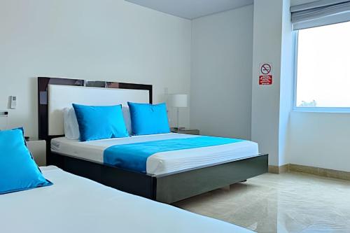 a bedroom with two beds with blue pillows and a window at Hotel Lotto Boutique in Cali