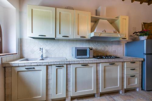 a kitchen with white cabinets and a sink and a microwave at Podere La Querciola in Guardistallo