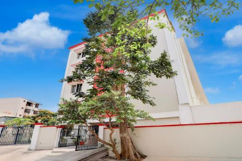 a tree in front of a white building with pink flowers at Super Collection O Bhanugudi Junction Kakinada Formerly Stay Inn Luxury in Kākināda