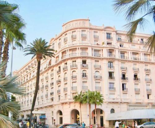 un grand bâtiment avec des palmiers devant dans l'établissement MIRAMAR-Studio tout confort sur la croisette, à Cannes