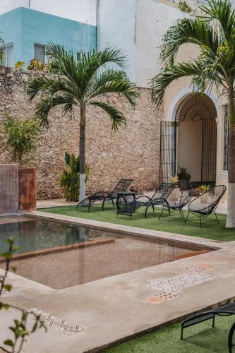 a pool with benches and palm trees next to a building at Hotel Boutique La Casona by Kavia in Mérida