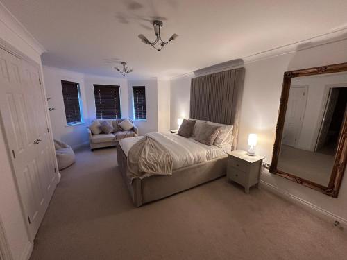ein Schlafzimmer mit einem Bett, einem Spiegel und einem Stuhl in der Unterkunft Elegant 5 Bed 5 Bath Home in Englefield Green