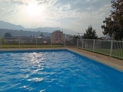 une piscine bleue avec une clôture et des montagnes dans l'établissement Meublé 3 étoiles - PISCINE- BALCON - TENNIS, à Aix-les-Bains